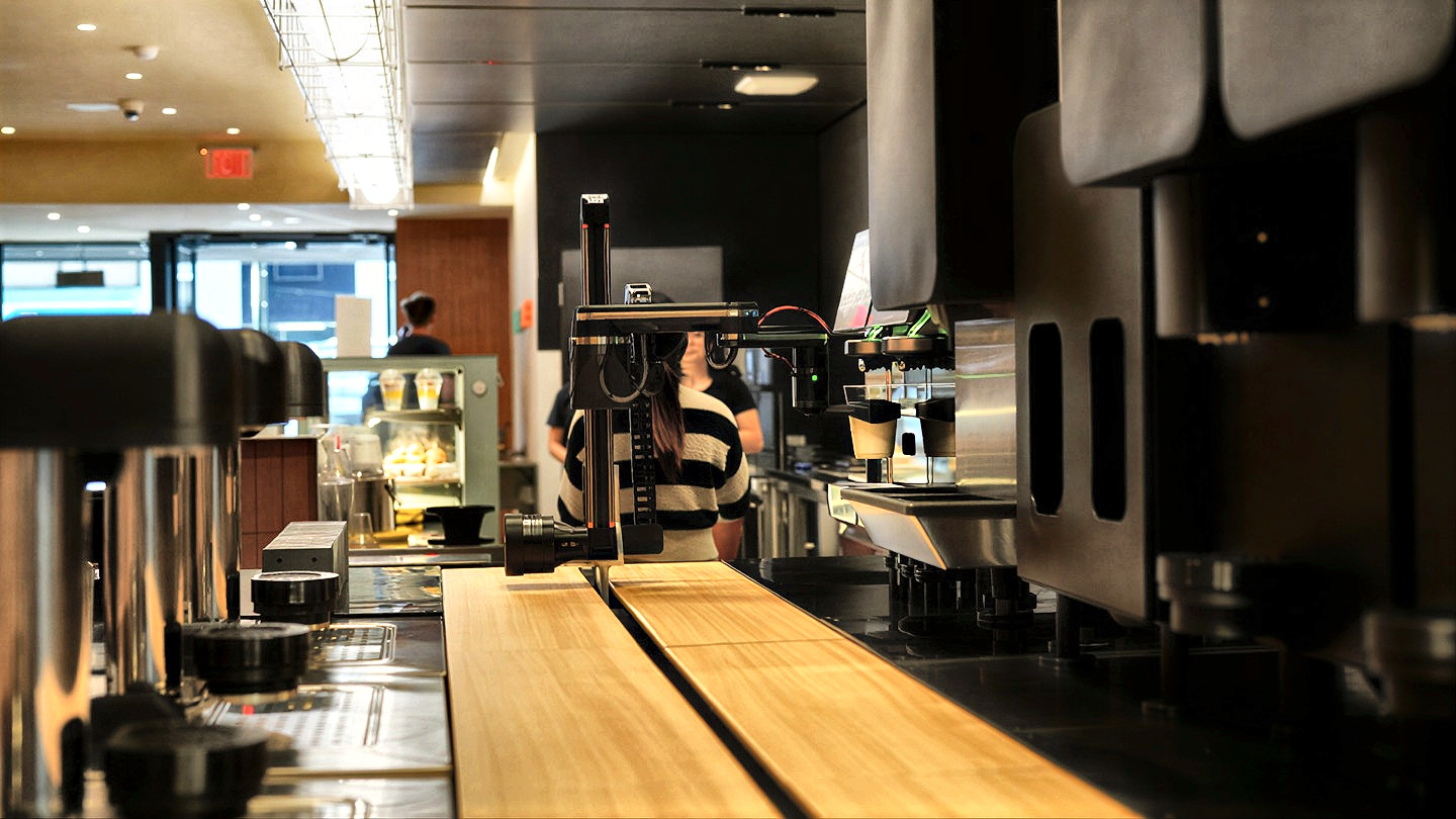 A Yummy Future barista works the counter beside the robot arm