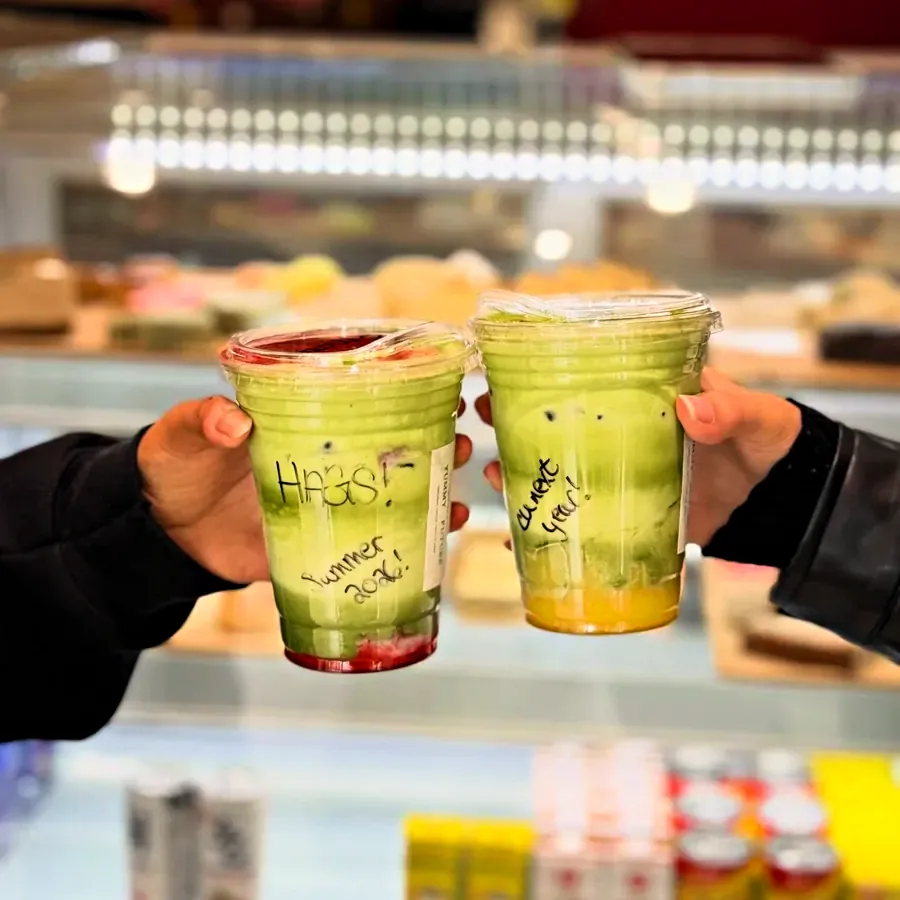 Two matcha drinks held up in front of the pastry case at the counter