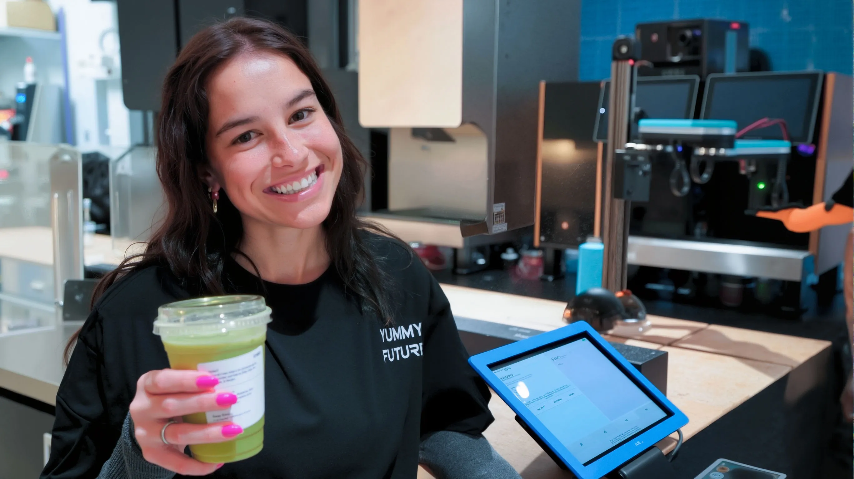 A staff member holding a matcha drink beside the robot and its ordering tablet